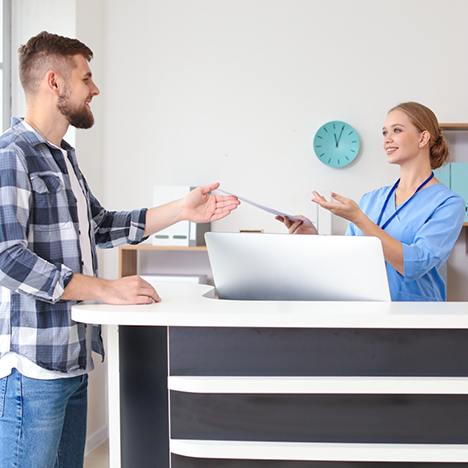 Dental team member at front desk handing form to male patient
