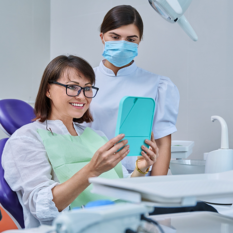 Female dental patient with glasses holding mirror