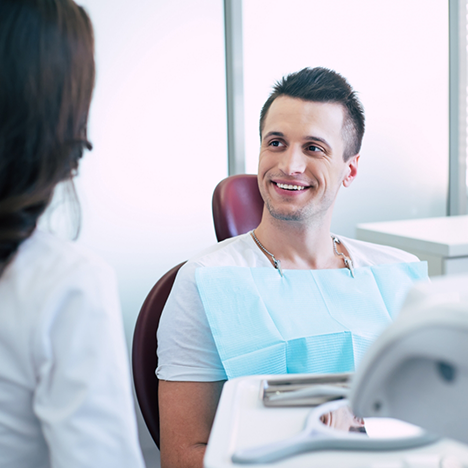 Man in dental chair smiling up at female dental patient