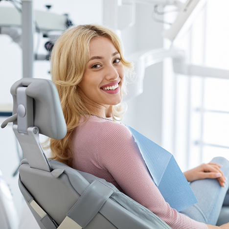 Woman in pink shirt leaning back in dental chair smiling