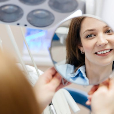 Woman looking at her smile in mirror after BioClear treatment