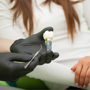 Close-up of hand with black glove holding a dental implant