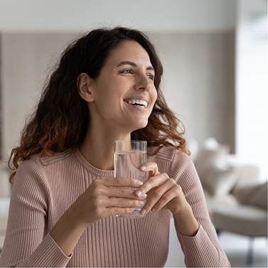 Woman in sweater holding glass of water and smiling
