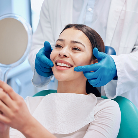 Woman in dental chair checking smile in handheld mirror