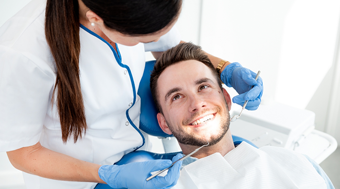 Man in dental chair smiling while female dentist examines his teeth