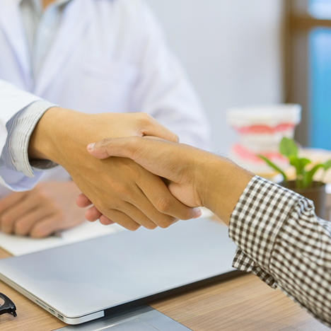 Shaking dentist's hand over desk with laptop