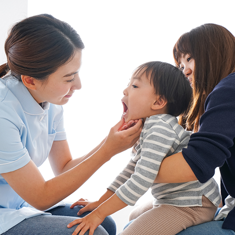 Child held by mother having teeth checked by dentist