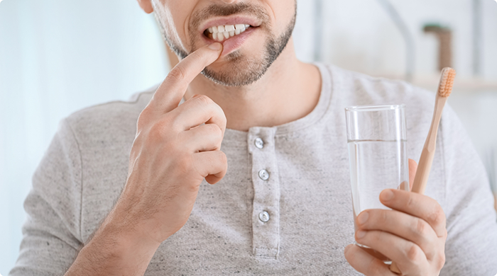 Man holding glass of water and toothbrush while pulling down lip