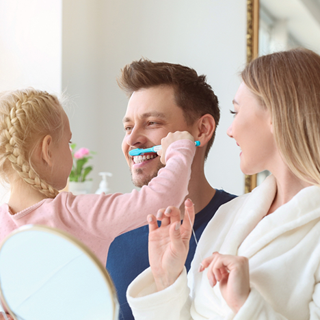 Man letting daughter brush his front teeth
