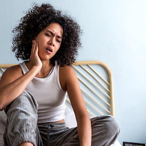Woman sitting on bed rubbing jaw in pain