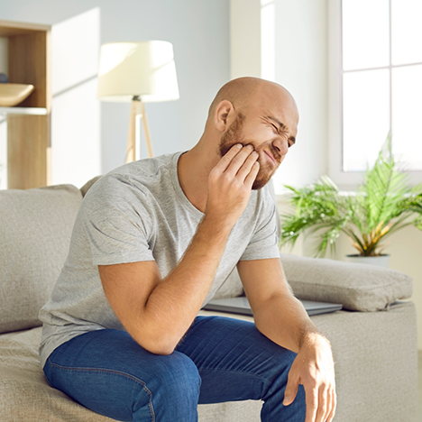 Man in grey shirt rubbing jaw in pain