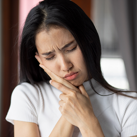 Woman in white sweater rubbing jaw in pain