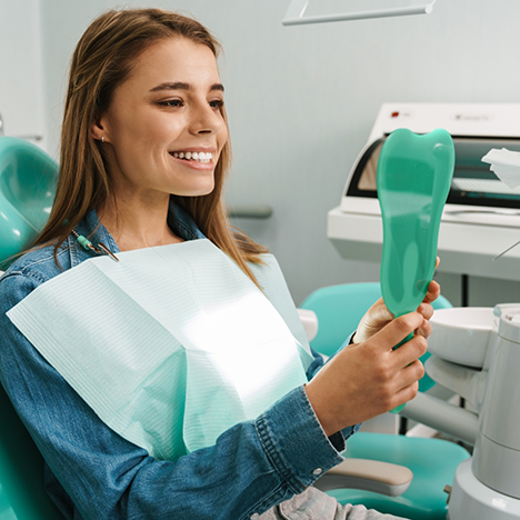 Woman sitting in dental chair checking smile in mirror