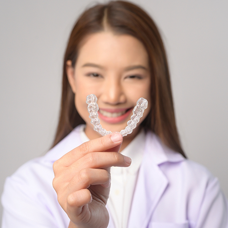 Smiling woman holding Invisalign clear aligner