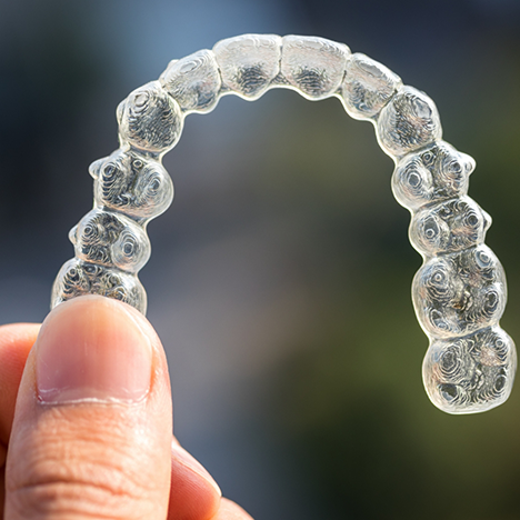 Invisalign clear aligner held between finger and thumb