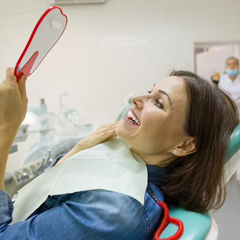 Woman in dental chair checking new smile in mirror