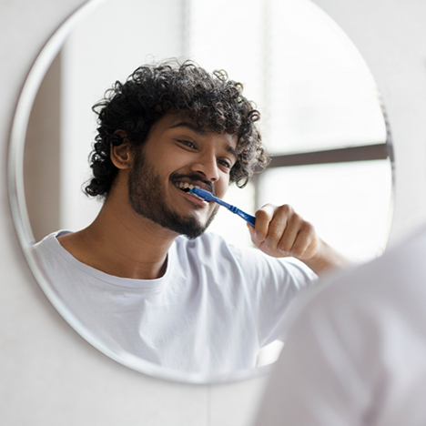 Man in white shirt brushing his teeth in the bathroom mirror