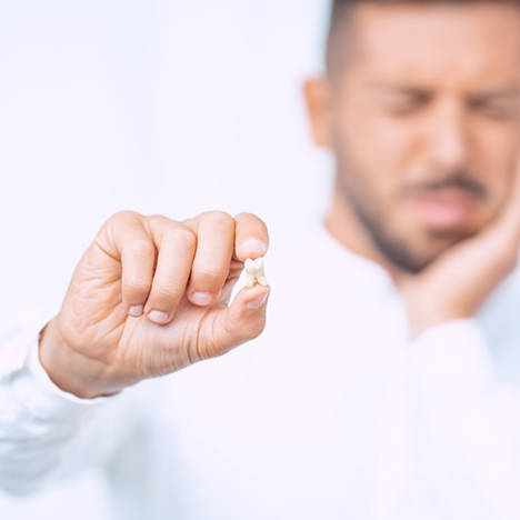Man rubbing jaw in pain and holding tooth