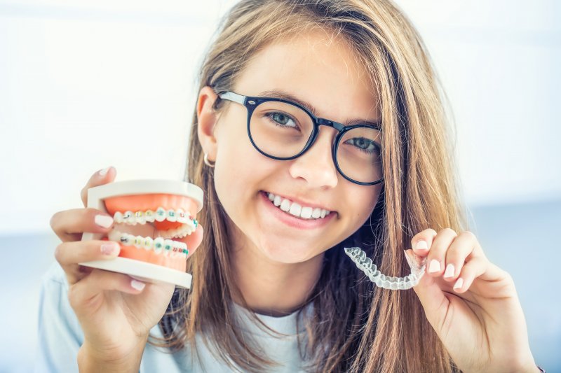 A girl holding an Invisalign tray in one hand and mock braces in the other